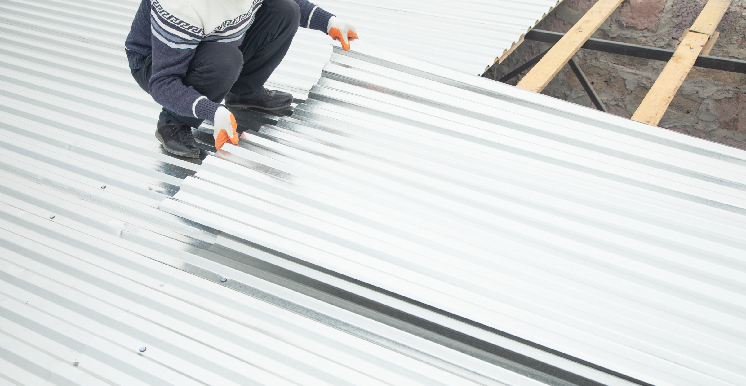 Worker puts the metal tiles on the roof of a house.